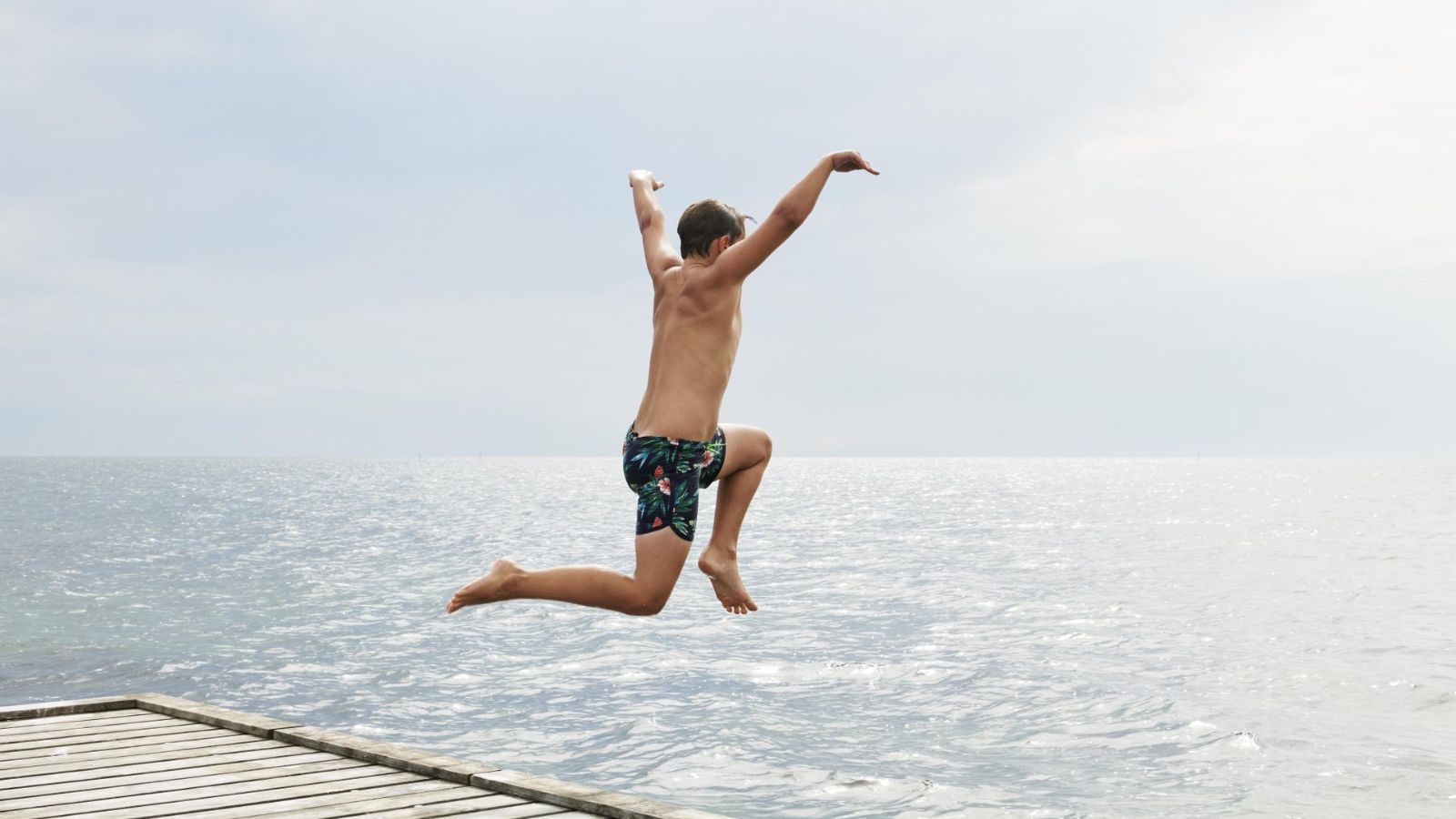 Dreng hopper i vandet fra en badebro